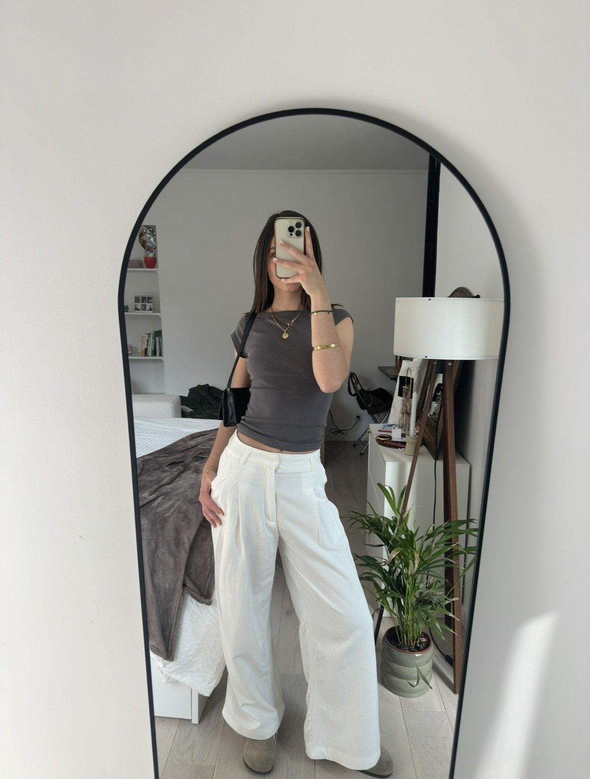 A fitted charcoal cap-sleeve top is styled with wide white pleated trousers, taupe boots, a black shoulder bag, and gold jewelry.