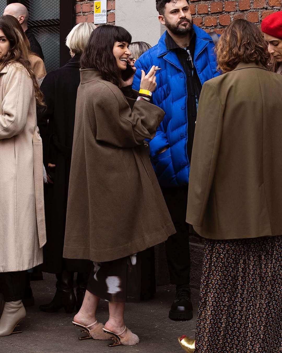 A central figure wears an oversized taupe-brown coat over a dark glossy midi skirt with pale fur-trim heeled mules.