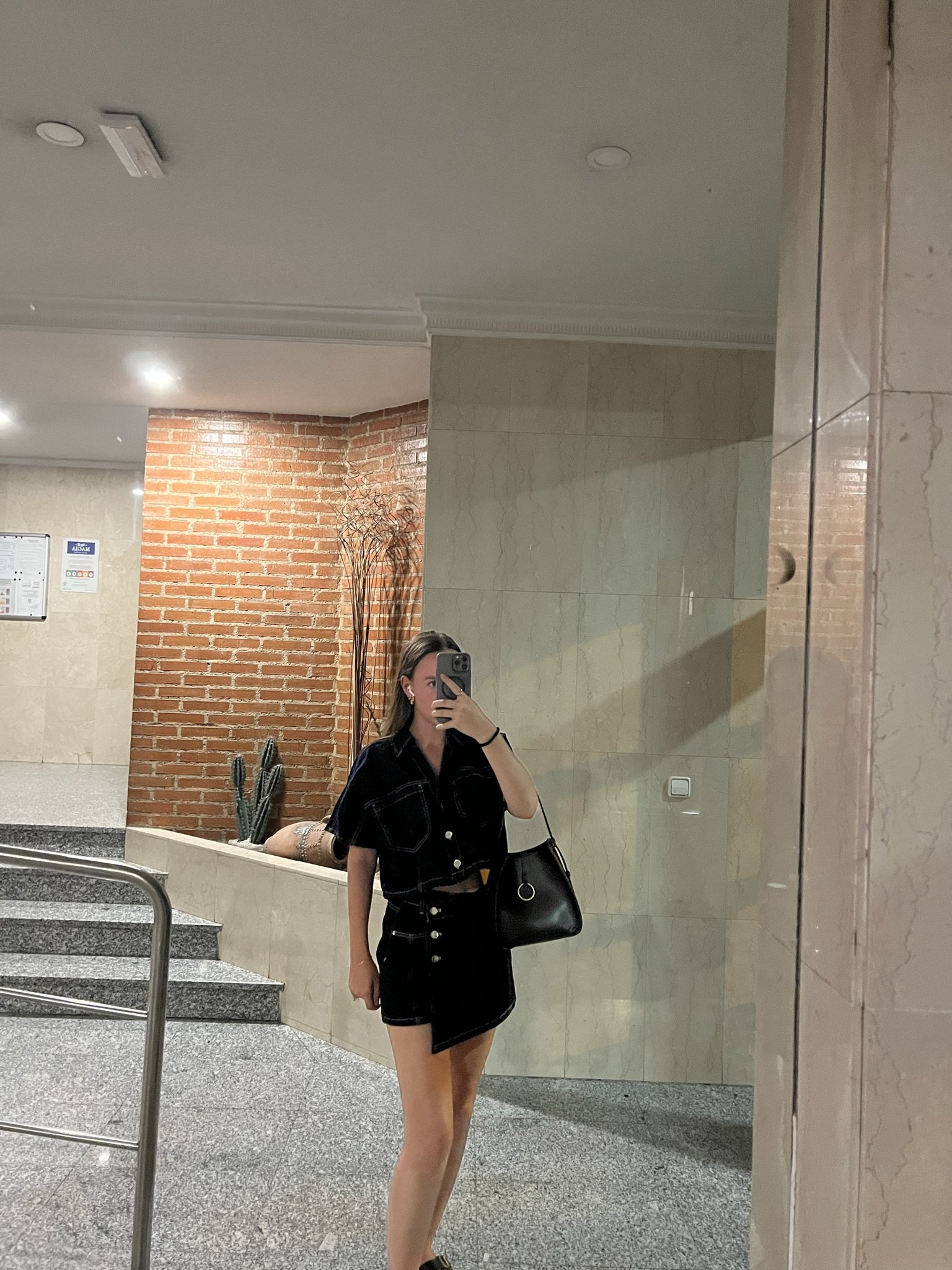 A black contrast-stitched short-sleeve top and matching mini skirt are styled with a black shoulder bag and dark shoes.