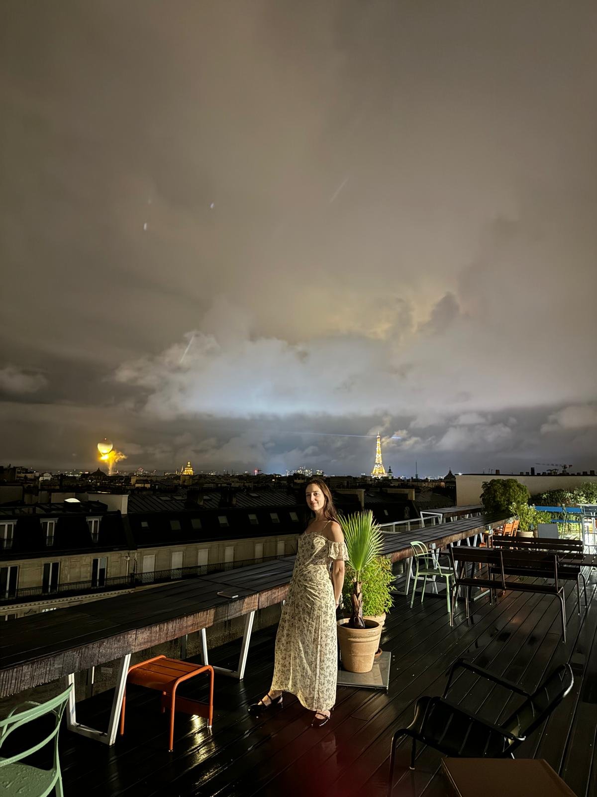 A cream floral off-shoulder maxi dress is styled with dark strappy heeled sandals on a nighttime rooftop.