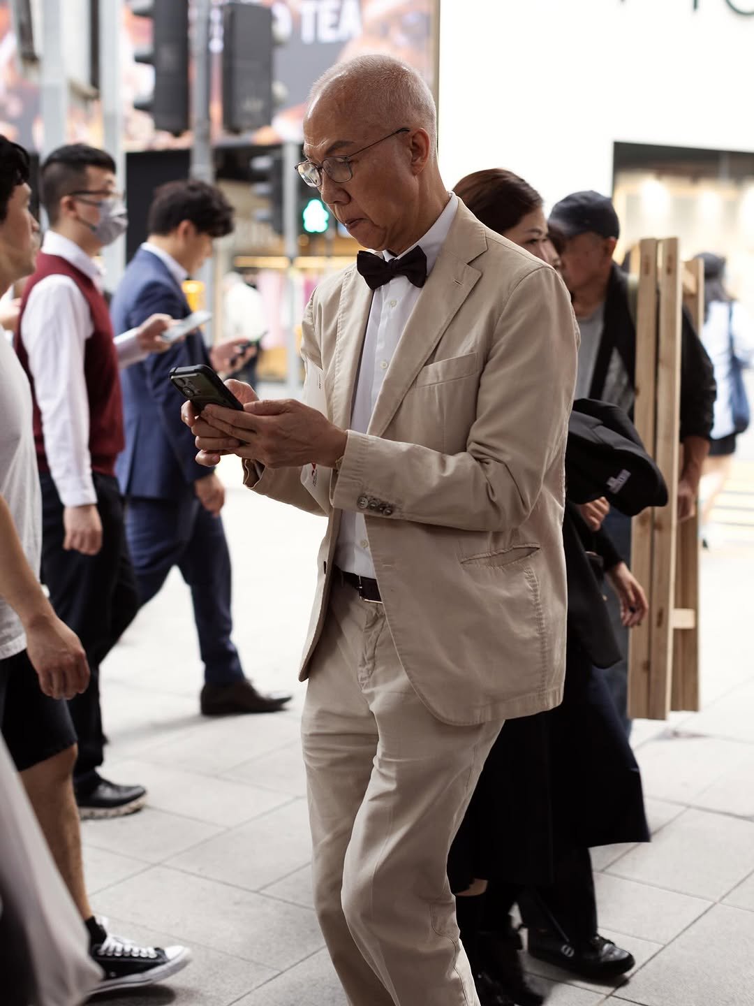 A beige suit is styled with a white shirt, black bow tie, black belt, and dark shoes.
