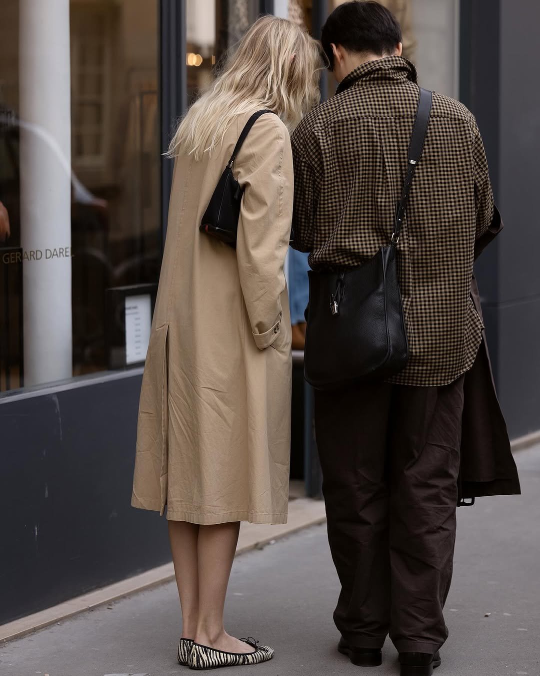 A beige knee-length trench coat is styled with a black shoulder bag and zebra-print flats beside a checked shirt look with dark trousers and a black crossbody bag.