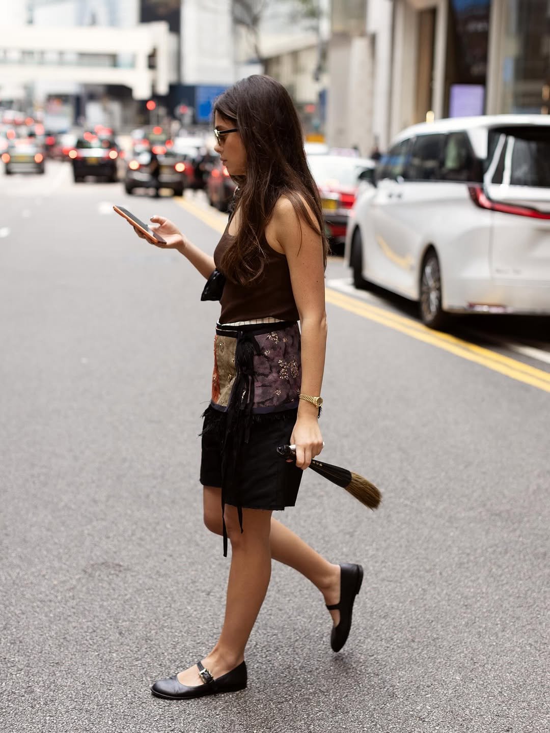 A brown sleeveless top is styled with patchwork shorts, black Mary Janes, sunglasses, and gold-toned jewelry.