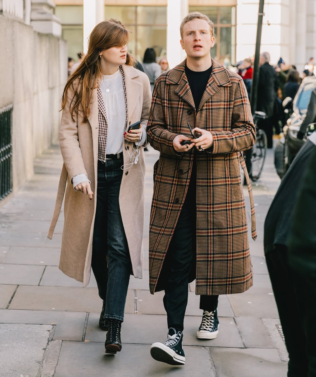 Two street-style looks pair long wool coats with dark trousers and black footwear, including a camel coat and a brown plaid belted coat.