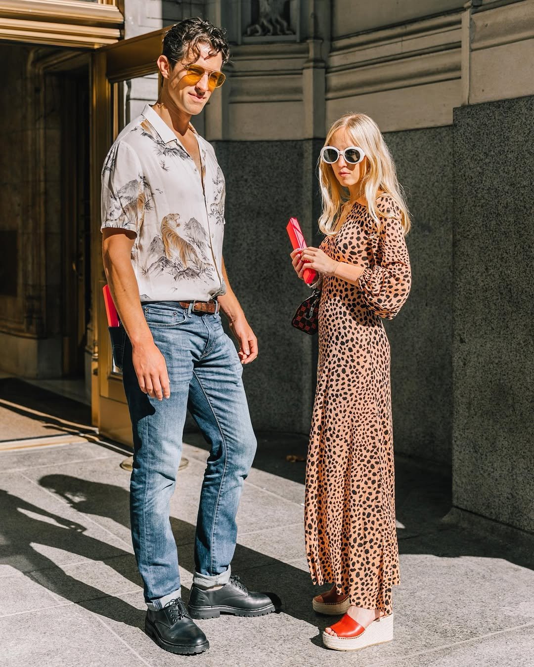 A street-style pair wears a printed camp shirt with cuffed jeans and a leopard-print maxi dress with bold sunglasses and platform sandals.