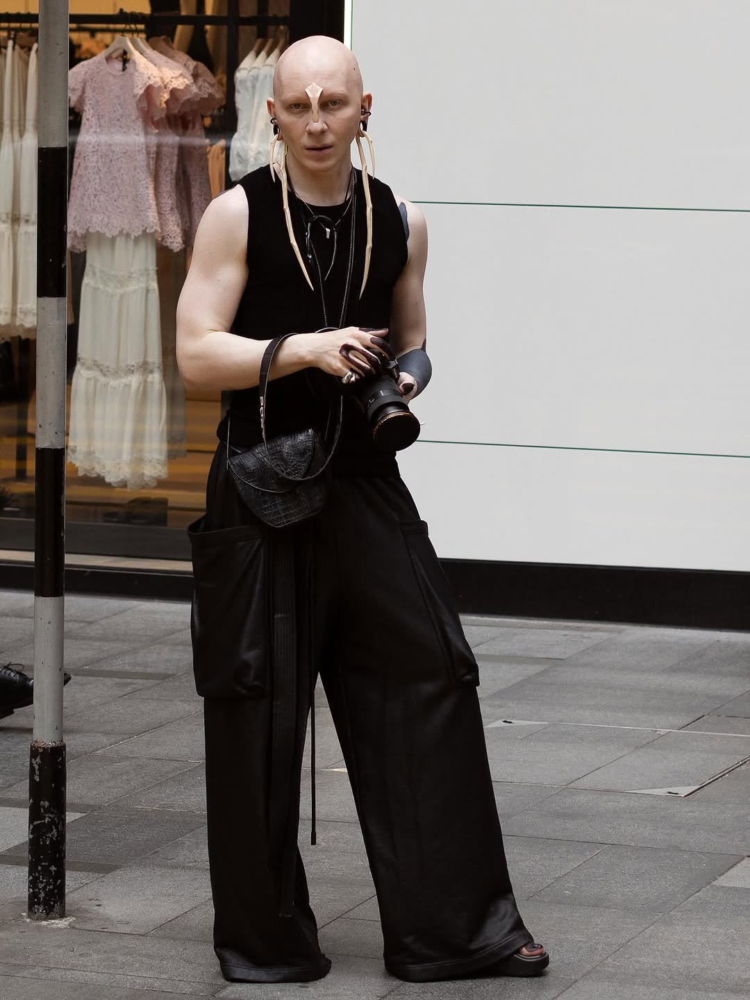 A black sleeveless top is styled with voluminous black wide-leg trousers, sculptural jewelry, and platform sandals.
