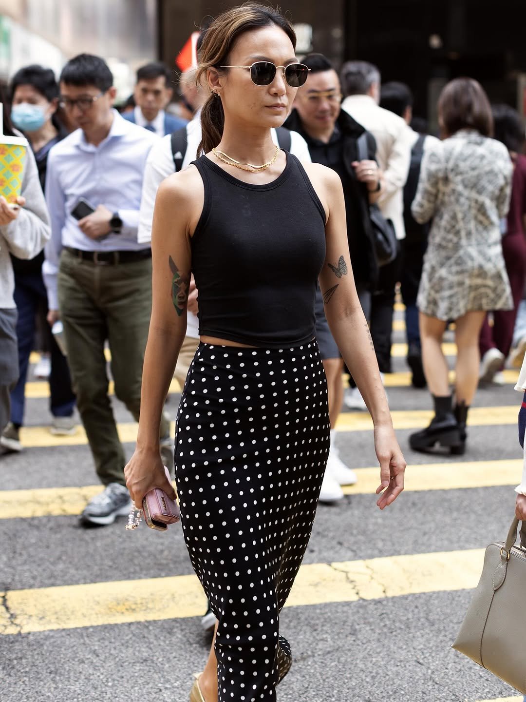 A black fitted tank is styled with a high-waisted black-and-white polka dot midi skirt, round sunglasses, gold jewelry, and a small pink clutch.