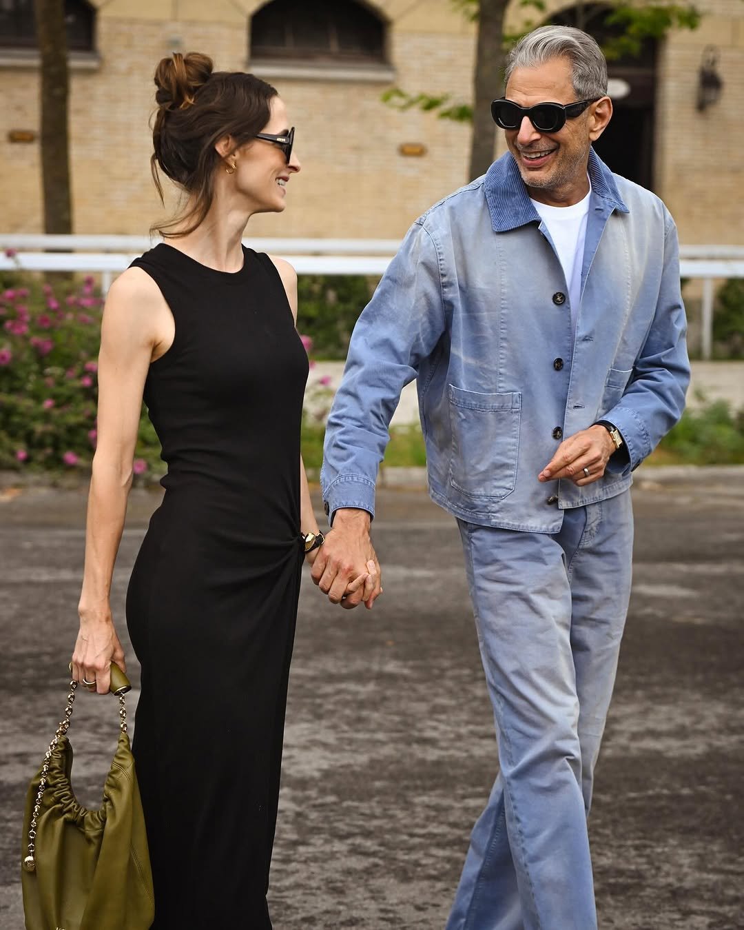 A black sleeveless column dress is paired with an olive ruched chain-strap bag beside a pale blue workwear-style jacket and trousers over a white tee.