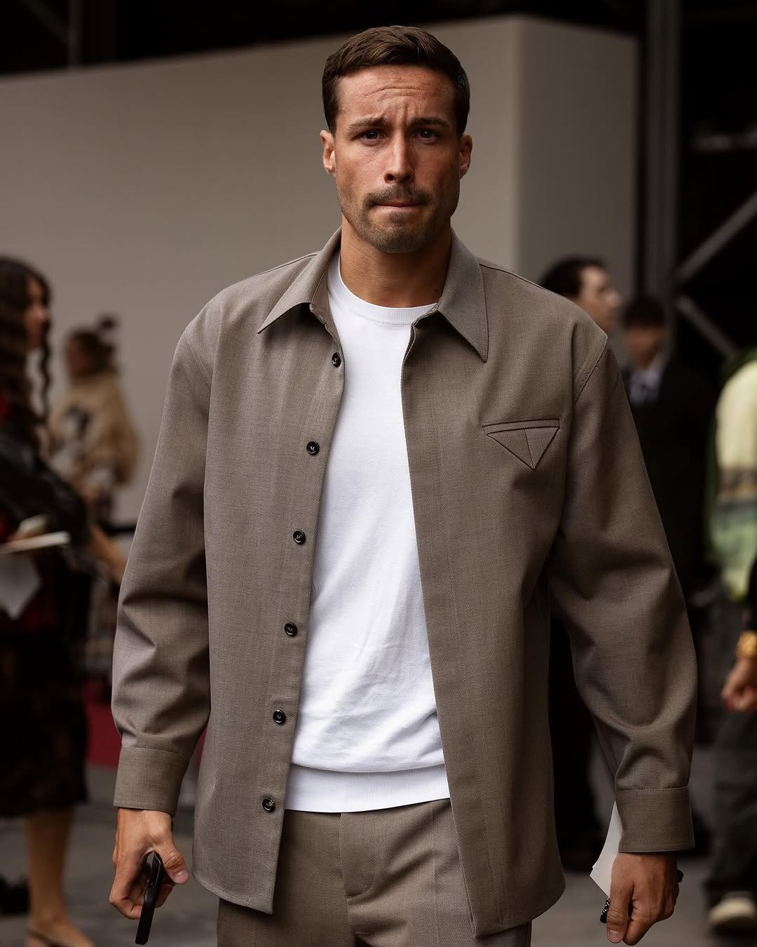A taupe overshirt and matching trousers are worn open over a plain white crew-neck sweatshirt.