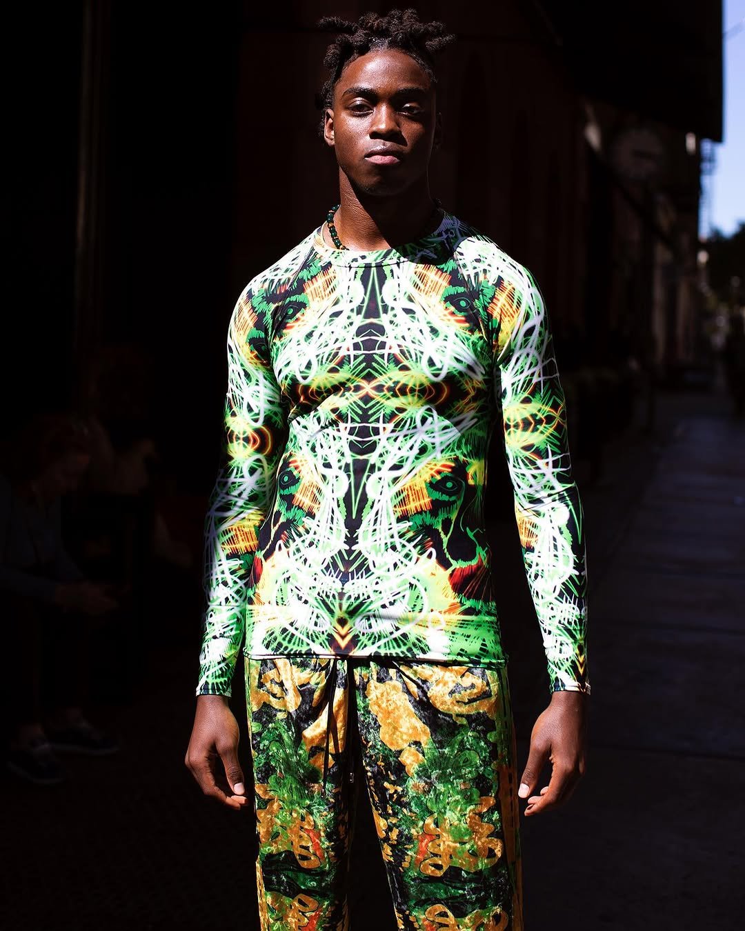 A fitted neon graphic long-sleeve top is paired with loose green-and-gold printed drawstring pants.