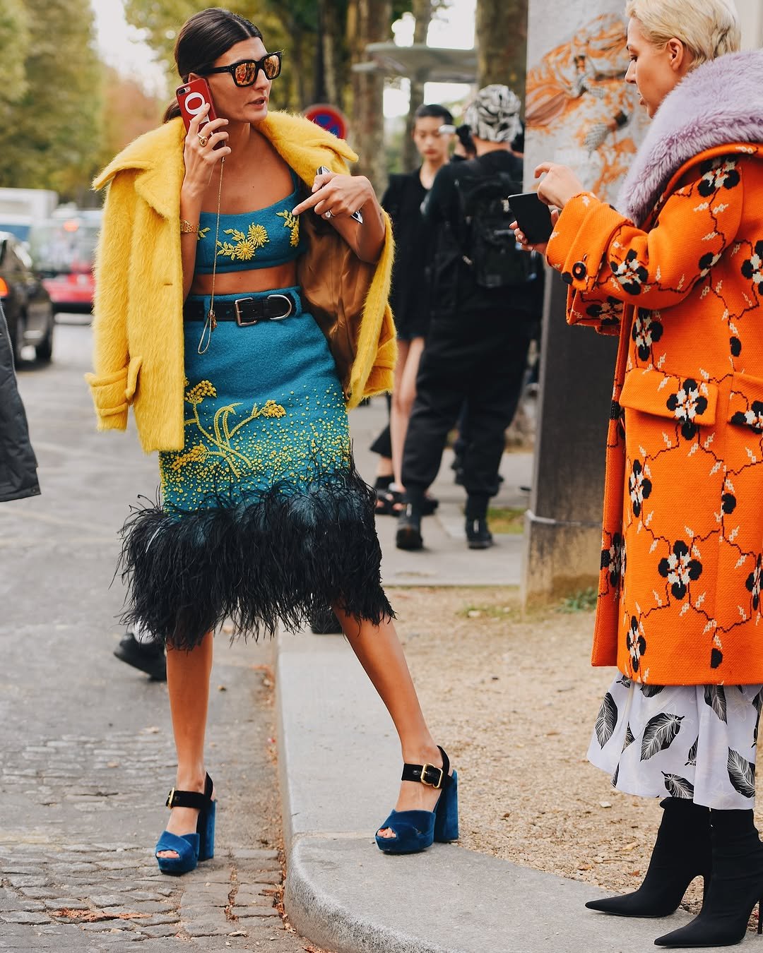 A teal embellished crop top and feather-trim skirt are styled with a bright yellow fuzzy coat, black belt, and blue platform heels.