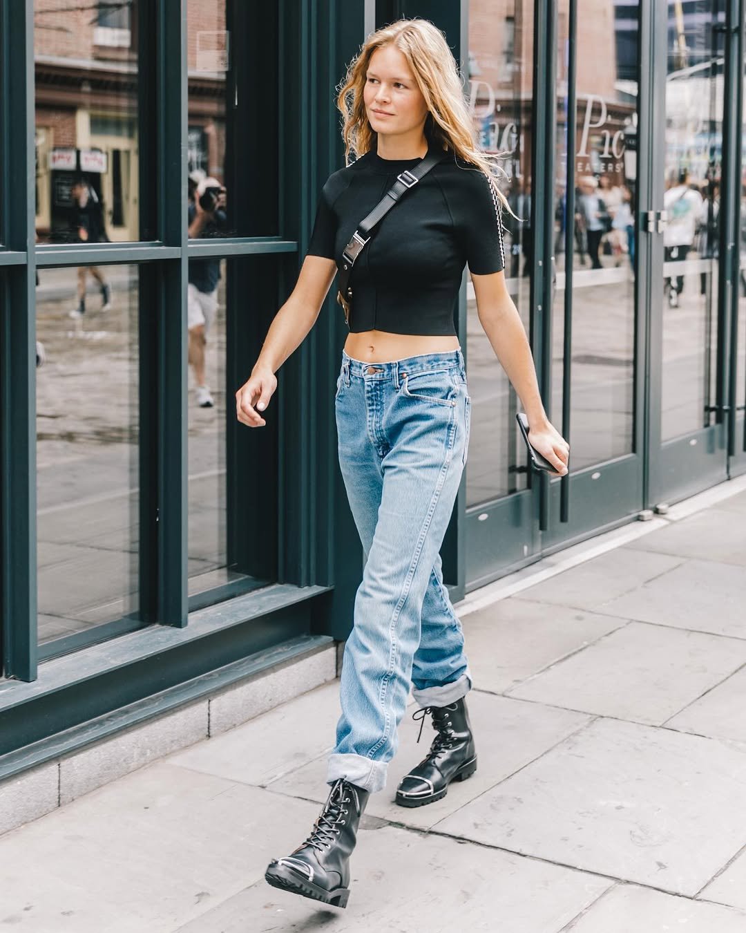 A fitted black cropped short-sleeve top is styled with light-wash cuffed jeans, black combat boots, and a black crossbody bag.