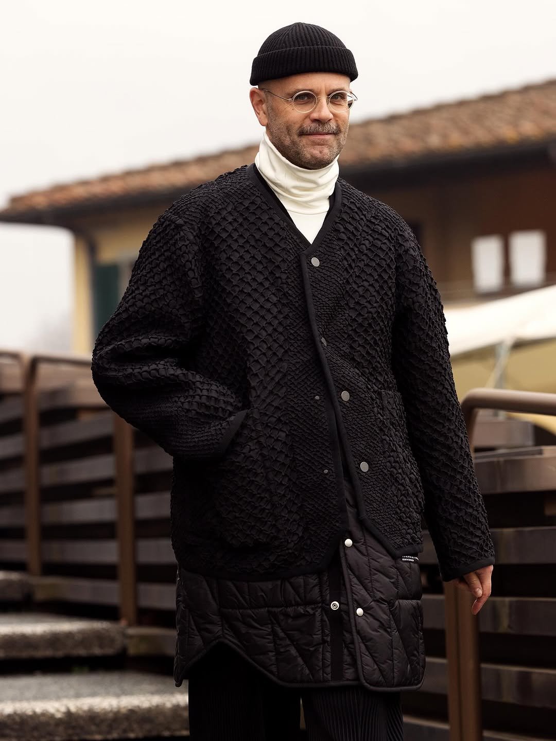 A black textured oversized cardigan is layered over a white roll-neck and black quilted longline layer with a black ribbed beanie.