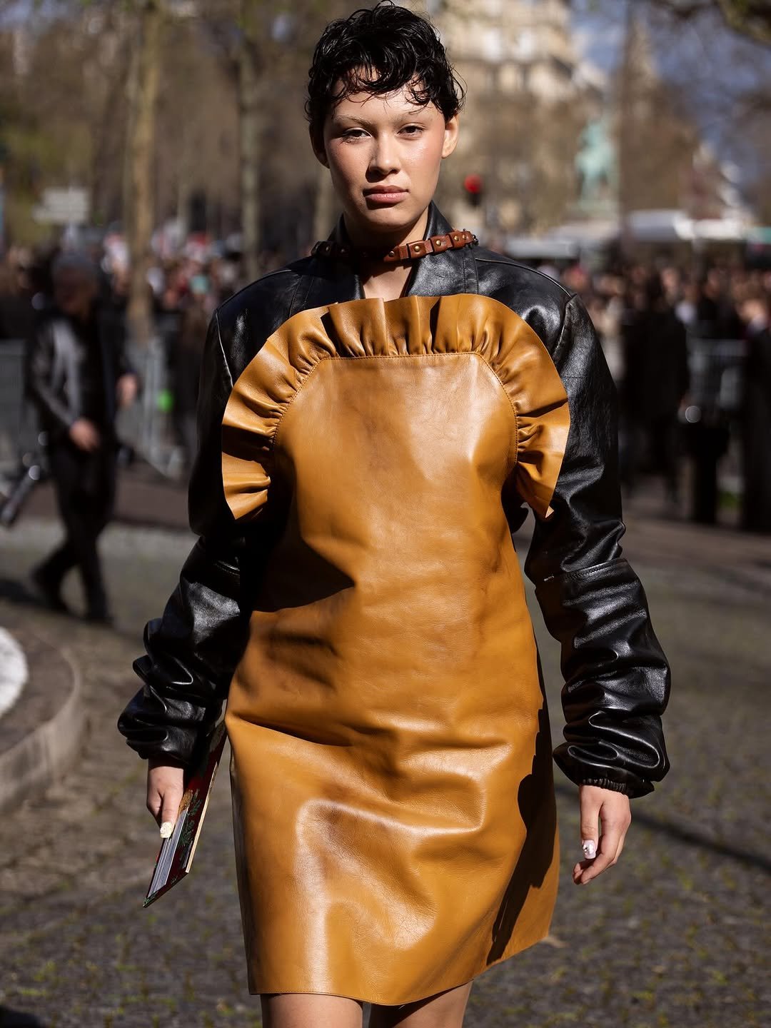 A tan leather mini dress with ruffled bib detail is layered over a black leather jacket and finished with a studded collar.