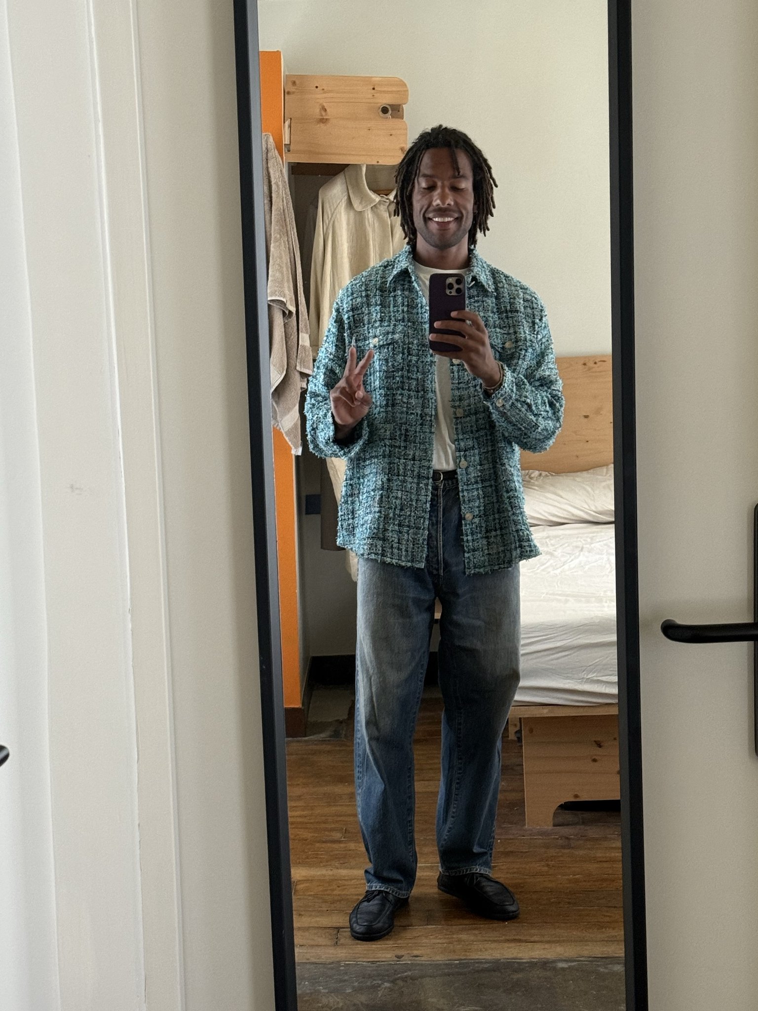 A teal textured overshirt is worn open over a white tee with relaxed blue jeans and black loafers.