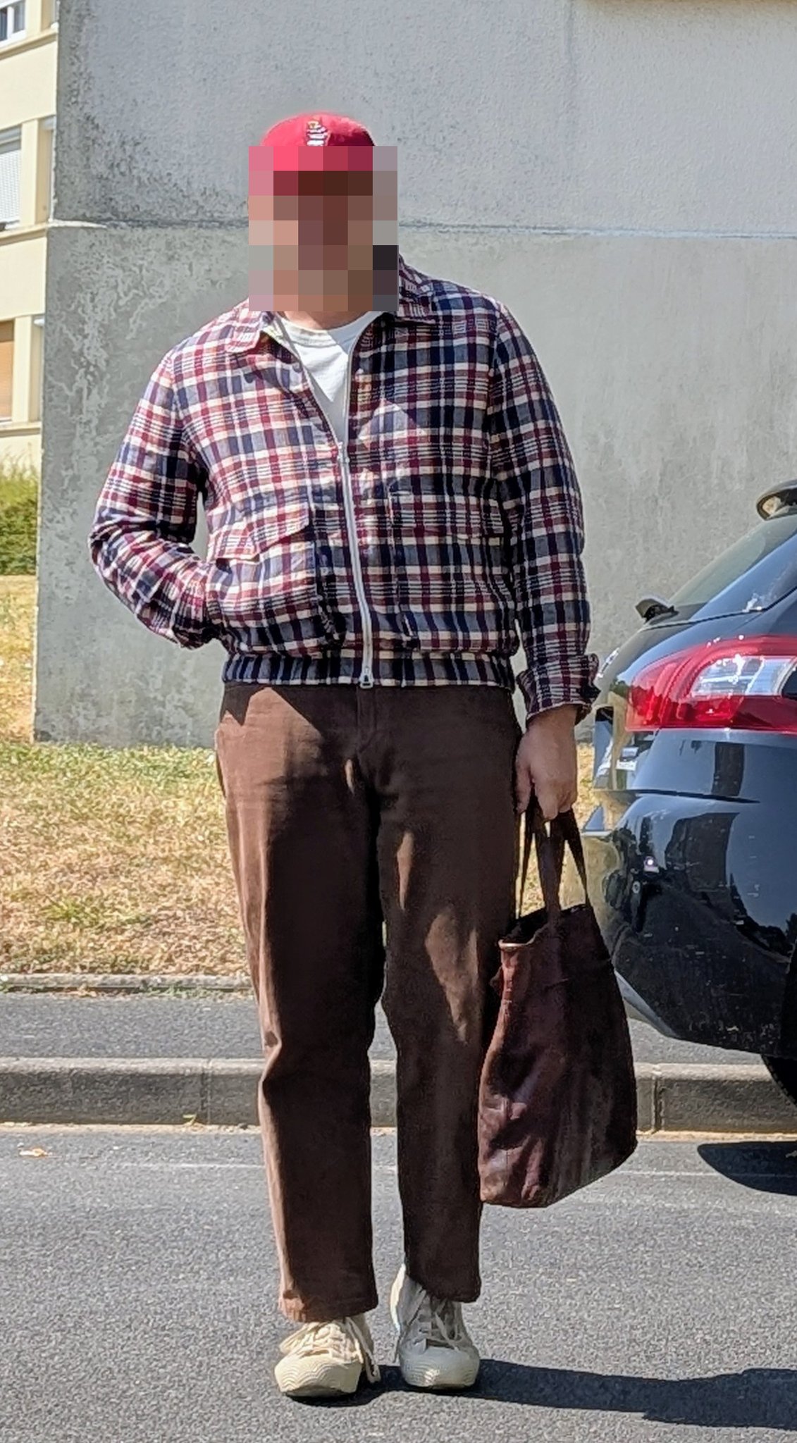 A plaid zip-front jacket over a white T-shirt is worn with brown cropped trousers, light sneakers, a red cap, and a dark tote.