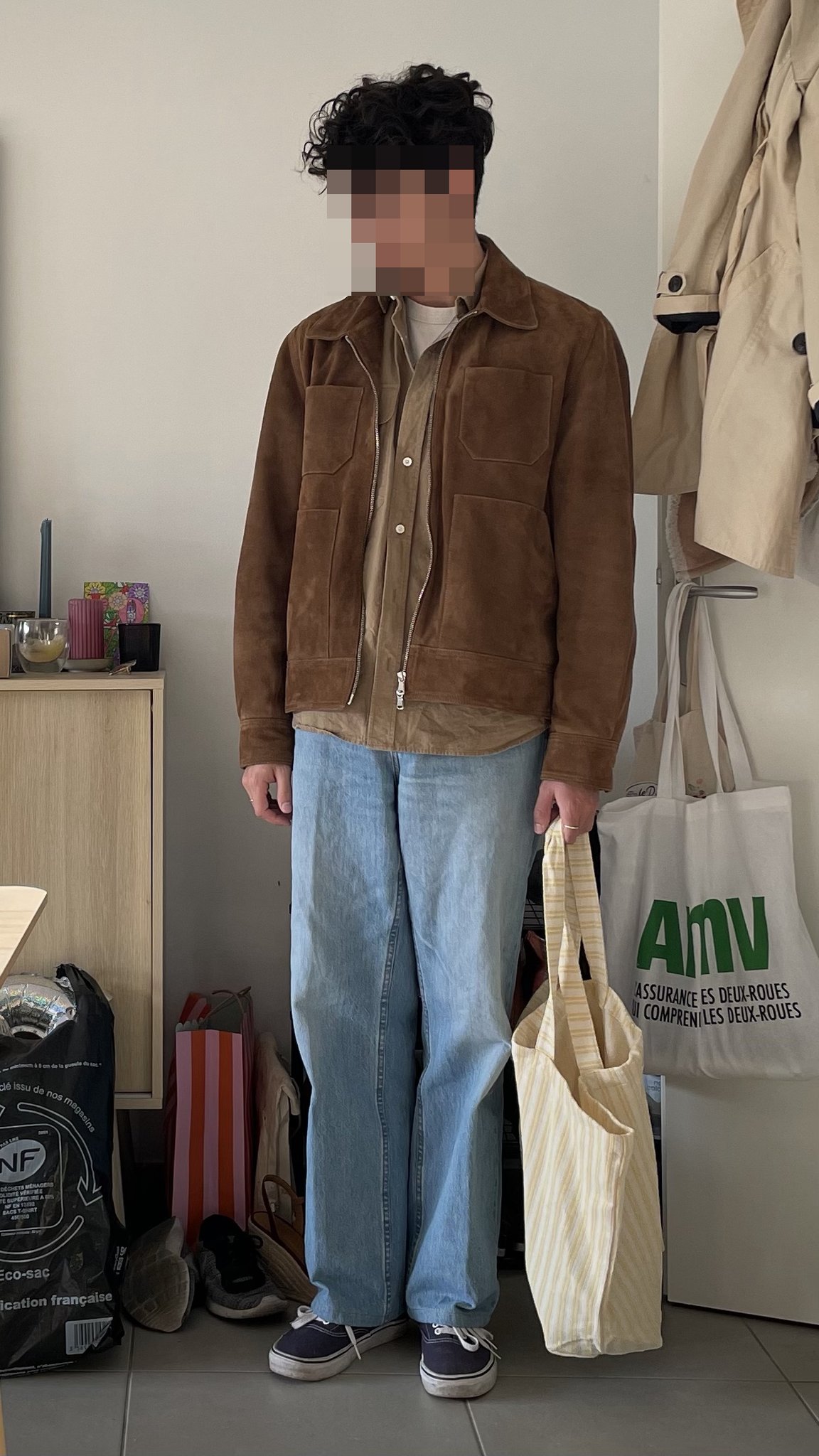 A brown suede zip jacket is layered over an olive shirt and white tee with loose light-wash jeans and dark canvas sneakers.