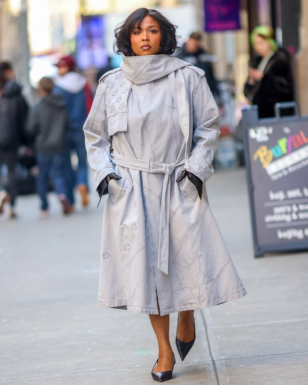 A light grey belted statement trench coat is styled with black pointed slingback heels and black gloves.