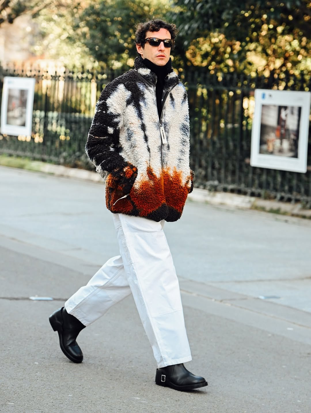A textured multicolor fleece jacket is styled with a black high neck, white wide-leg trousers, black boots, and dark sunglasses.